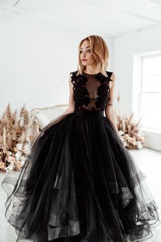 a woman standing in front of a white wall wearing a black dress with sheer detailing