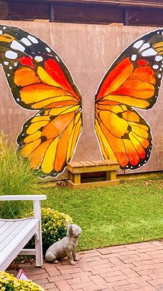 a large butterfly painted on the side of a building next to a bench and flowers