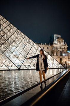 a woman is standing in front of the pyramid at night with her arms spread out