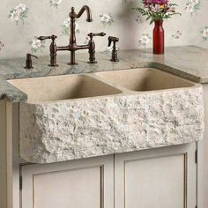 a stone sink with two faucets in front of it and flowers on the wall