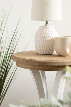 a white vase sitting on top of a wooden table next to a cup and saucer