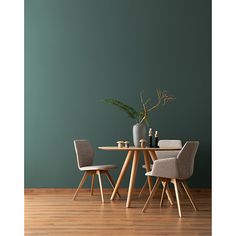 a dining table with two chairs and a vase on it in front of a green wall