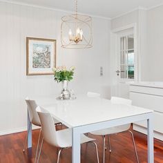 a white dining room table and chairs in front of an open kitchen area with wood flooring