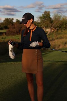 a woman holding a golf club and wearing a skirt