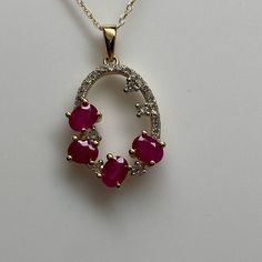 This Beautiful Gemstone And Diamond Cluster Pendant Has Four Natural Matching Rubies Prong Set Towards The Bottom Of The Oval Shape Charm. Each Ruby Is Oval Shape And Has A Medium Cherry Red Color. The Gemstones Weigh A Total Of 1.00ct Twt. There Is A Full Line Of Natural White Diamonds That Loop Around The Top Of The Charm And Connect The Two Outside Rubies. There Are Also A Few Additional Slightly Larger Diamonds Scattered Around The Inside. The Total Diamond Weight Is 0.18ct Twt. This Pendant Red Dazzling Necklace With Diamond Accents, Dazzling Red Necklace With Diamond Accents, Dazzling Red Necklaces With Diamond Accents, Red Necklace With Sparkling Round Stones, Red Ruby Necklace With Diamond Accents, Red Ruby Stone Setting Necklace, Red Ruby Necklaces With Diamond Accents, Red Pendant Necklace With Diamond Accents, Red Ruby Necklace With Stone Setting