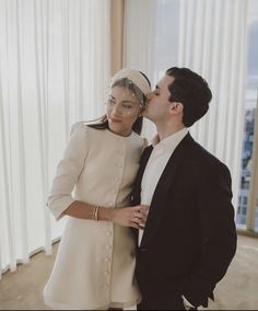 a man and woman standing next to each other in front of a window with white curtains