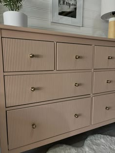 a dresser with many drawers and knobs on the bottom drawer, next to a plant