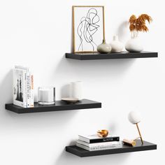 two black floating shelves with books, vases and other decorative items on them against a white wall