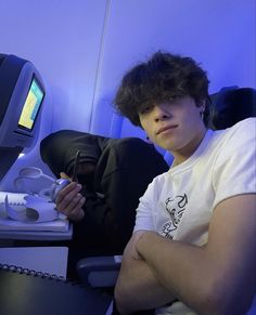 a young man sitting in an airplane with his arms crossed and looking at the camera