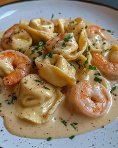 a white plate topped with pasta and shrimp covered in gravy, garnished with parsley