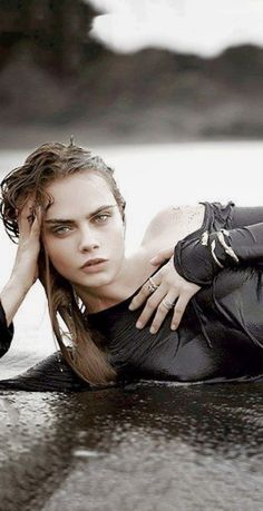 a beautiful woman laying on top of a body of water in wetsuit and black gloves