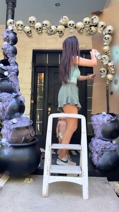 a woman standing on a stepladder in front of a door with skulls hanging from it