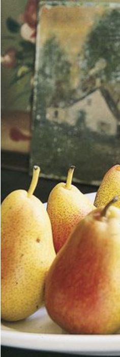 some pears and apples on a plate in front of a painting with an easel behind them