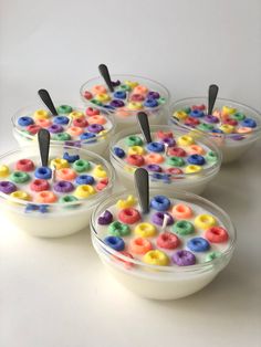 four bowls filled with different colored cereals on top of a white table next to each other