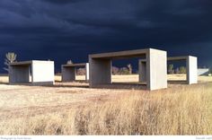 three concrete benches sitting in the middle of a field under a dark sky with storm clouds