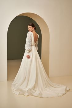 a woman in a white wedding dress is standing with her back turned to the camera