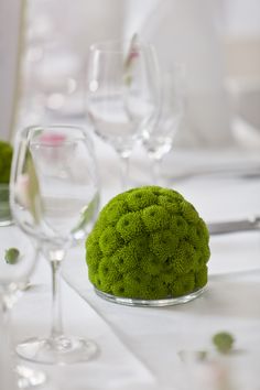 a green moss ball sitting on top of a table next to wine glasses