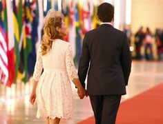 a man and woman holding hands while walking down a red carpeted hallway with flags in the background