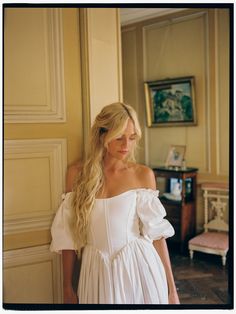 a woman in a white dress leaning against a wall