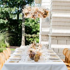 an outdoor dining table set up with white linens and gold place settings for dinner