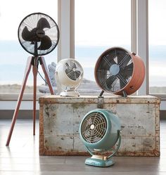 three fans sitting on top of an old suitcase in front of a window with large windows