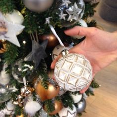 a hand holding an ornament in front of a christmas tree with ornaments on it