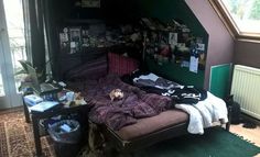 an unmade bed sitting in the corner of a room with lots of clutter