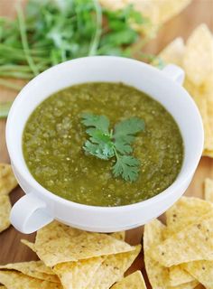 a white bowl filled with green salsa surrounded by tortilla chips