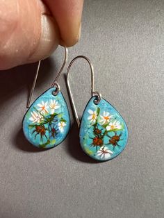 a pair of blue earrings with flowers painted on the inside of them, being held by a person's hand