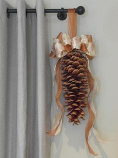 a pine cone hanging on the side of a curtain with ribbon attached to it,