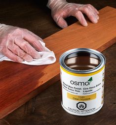 a person with white gloves on is cleaning a wooden surface next to a can of brown paint