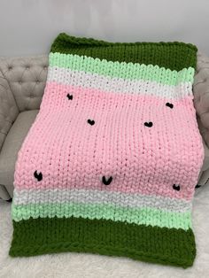 a pink and green knitted blanket sitting on top of a couch next to a pillow