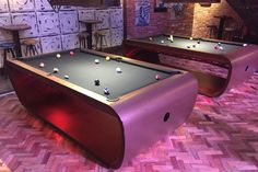 two pool tables with balls on them in a room that has brick walls and wood flooring