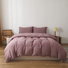 a bed with pink linens and pillows in a white room next to a wooden chair