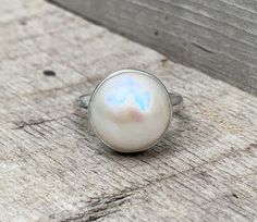 This elegant and stately pearl ring is made from a beautiful and unique white cream 14mm Mabe South Sea AAA Pearl that has many hues including pink. The pearl has been set in sterling silver with a sterling silver ring band handmade from half dome wire. This ring has some height, the setting is almost 1/2 inch high. The white cream pearl is more matte than the other mabe pearls listed, but still has a luminescent quality that makes it captivating!Made to order! Choose your size and your color pe White Mother Of Pearl Wedding Ring, Classic Mother Of Pearl Ring As Gift, Classic Mother Of Pearl Ring For Gift, Classic Mother Of Pearl Ring As A Gift, Wedding Pearl Ring In Mother Of Pearl, Wedding Pearl Ring With Mother Of Pearl, White Mother Of Pearl Round Pearl Ring, White Mother Of Pearl Rings, White Pearl Drop Ring