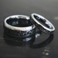 two wedding rings with black diamonds on them sitting on top of a table next to each other