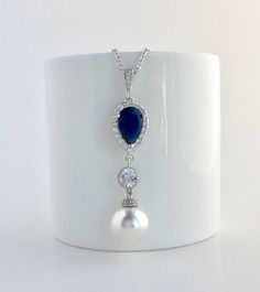 #Classic pearl bridal necklace and pendant set with rhodium plated brass peg and bail. Necklace features a halo blue sapphire crystal teardrop pendant with a 12mm Swarovski single pearl drop that dangles from round rhodium plated cubic zirconia connector and bail. Length of the rhodium plated chain is 18 inches and comes with 2 inches extender and lobster clasp. For matching earrings click: https://www.etsy.com/listing/578469918/blue-bridal-earrings-sapphire-wedding?ref=shop_home_active_3 For co Sapphire Pendant Necklace For Wedding, Blue Sterling Silver Pearl Necklace Gift, Blue Dangle Necklaces For Wedding, Blue Pearl Drop Wedding Jewelry, Blue Pearl Drop Jewelry For Wedding, Sapphire Drop Necklace For Wedding, Elegant Sapphire Bridal Necklace For Wedding, Elegant Sapphire Bridal Necklace, Formal Blue Pearl Drop Necklace