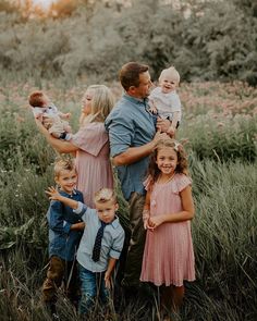 a group of people standing in the grass with one holding a baby and two children