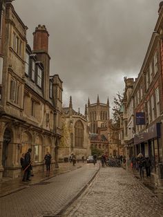 people are walking down the cobblestone street in an old european city with tall buildings