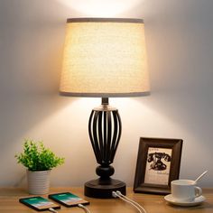 a table with a lamp and cell phone on it next to a potted plant