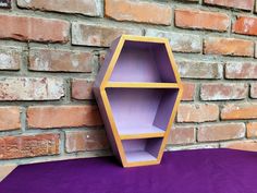 a purple shelf sitting on top of a purple rug next to a brick wall with a yellow hexagon shaped shelf