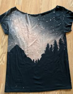 a black t - shirt with trees and stars on it sitting on a wooden floor