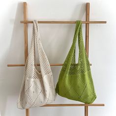 two purses hanging on a wooden rack in front of a white wall, one green and the other beige