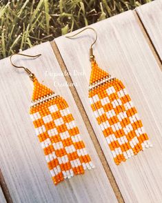 the orange and white beaded earrings are hanging from wood planks with grass in the background