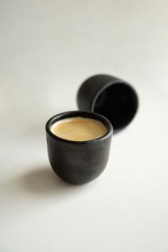 two black cups sitting next to each other on a white counter top with one cup filled with liquid