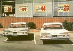 two old cars are parked in front of a grocery store with advertisements on the windows