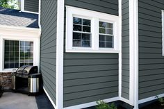 a gray house with white trim and two windows on the side, next to a trash can