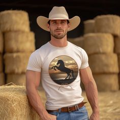 Experience the beauty of the wild west with this Rearing Horse at the Beach tee. Featuring a majestic rearing horse against a stunning backdrop of sun, sand, and surf at sunset, this unique design brings a bold western vibe to any look. Be the envy of the town! Horse At The Beach, Country Husband, Cowboy Pics, Cowboy Outfit For Men, Cowboy Attire, Coastal Western, Cowboy Outfit, Rearing Horse, Mens Haircuts Short Hair