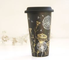 a black coffee cup with dandelions painted on it