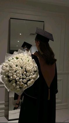 a woman holding a bouquet of white flowers in front of a mirror with her graduation cap on